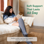 Woman seated on a sofa reading while wearing gray knee-high bamboo compression socks.